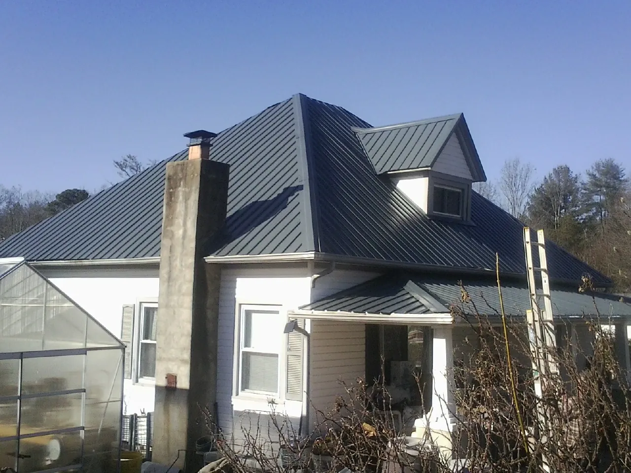 Dark blue standing seam metal roof on a white farmhouse with dormer — Slate & Tile Roof Repair by Roofing Brothers in Carr