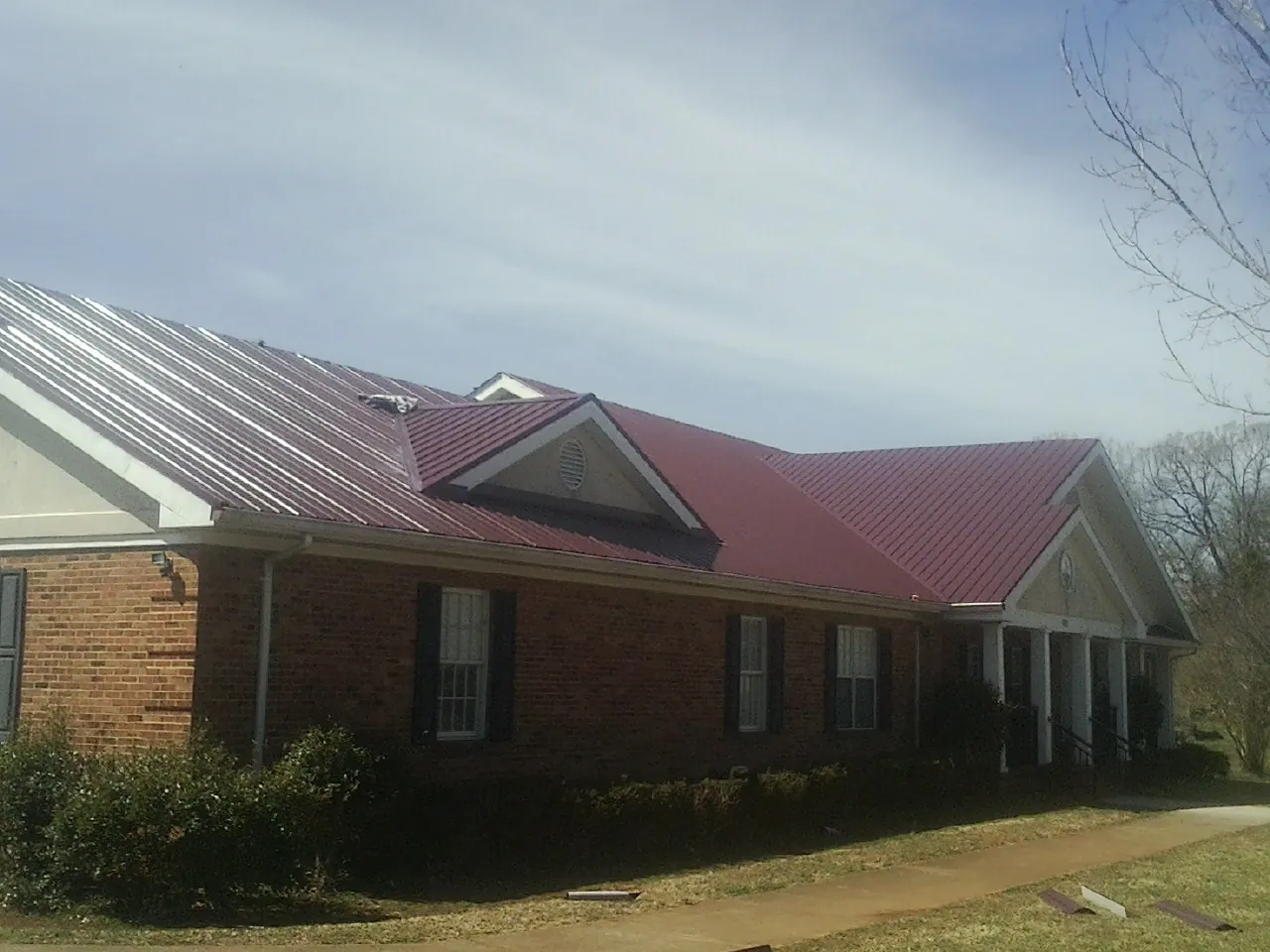 Red metal roof with gabled entries on a long brick building, from a Hail Damage Roof Repair job in Carr