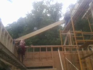 Carpenter raising a rafter beam on a new second story frame in Carr