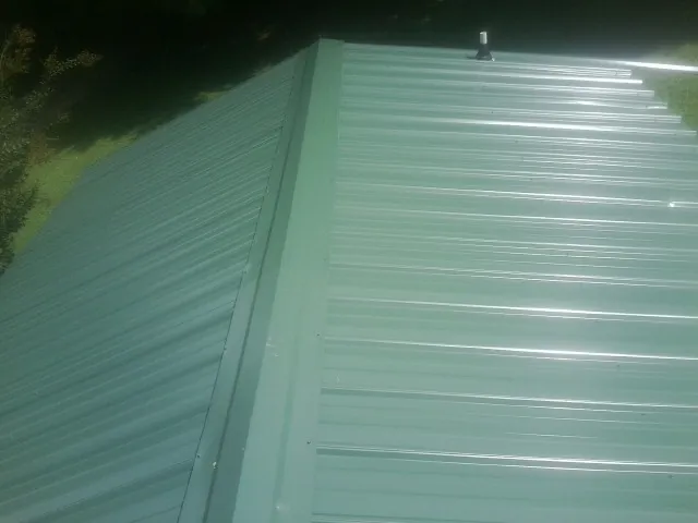 New green metal panels meeting at the ridge of a roof — Flat Roof Repair work by our crew in Carr
