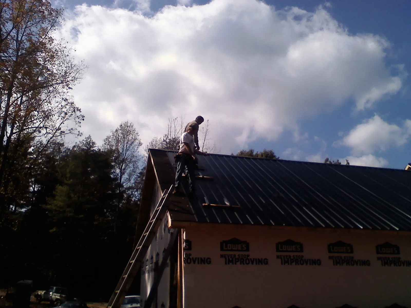 Roofer fastening dark metal panels high against a cloudy sky, from a Roof Inspection job in Carr