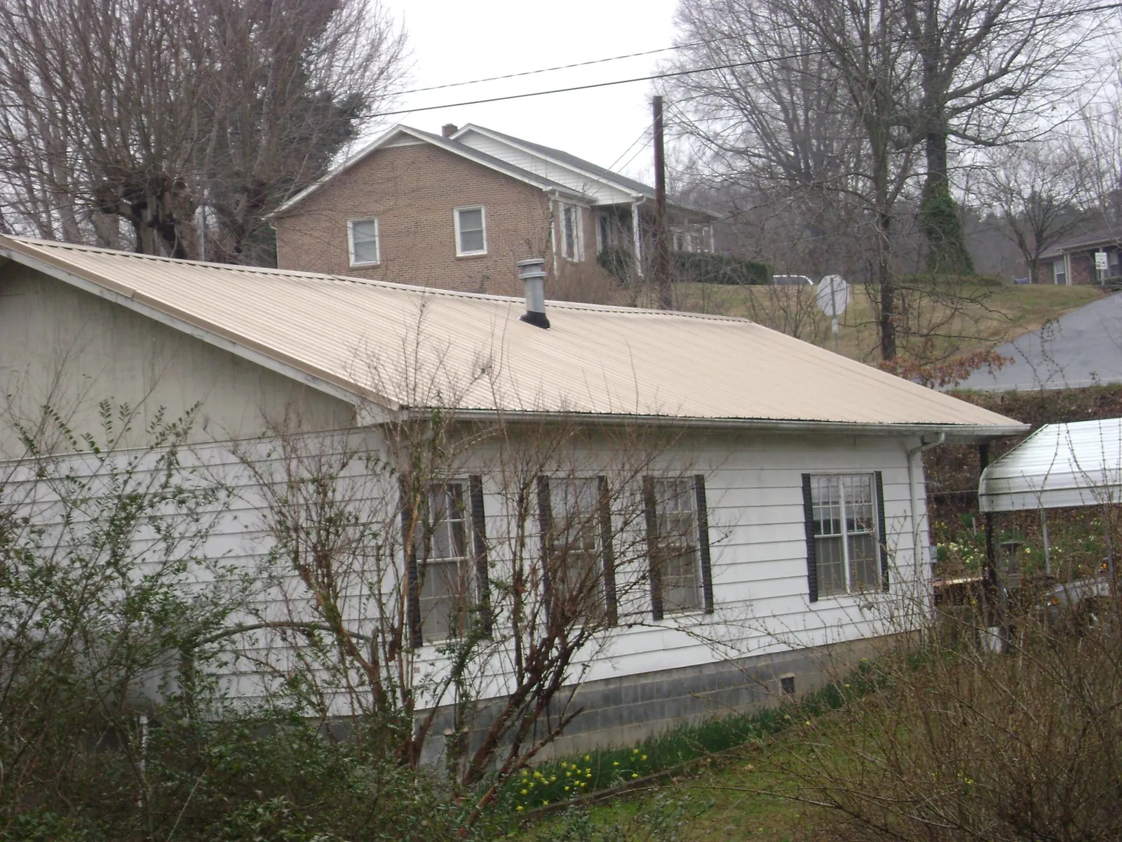 Tan metal roof on a white sided house set into a hillside — Commercial Roofing by Roofing Brothers in Carr